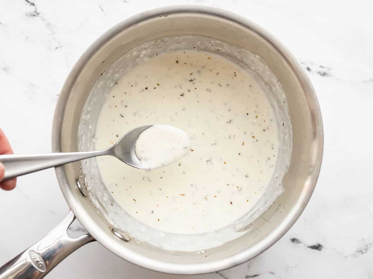 Finished herby white sauce on a spoon in the sauce pot