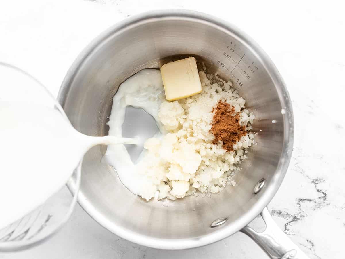 cauliflower, butter, and spices in a sauce pot, milk being poured in
