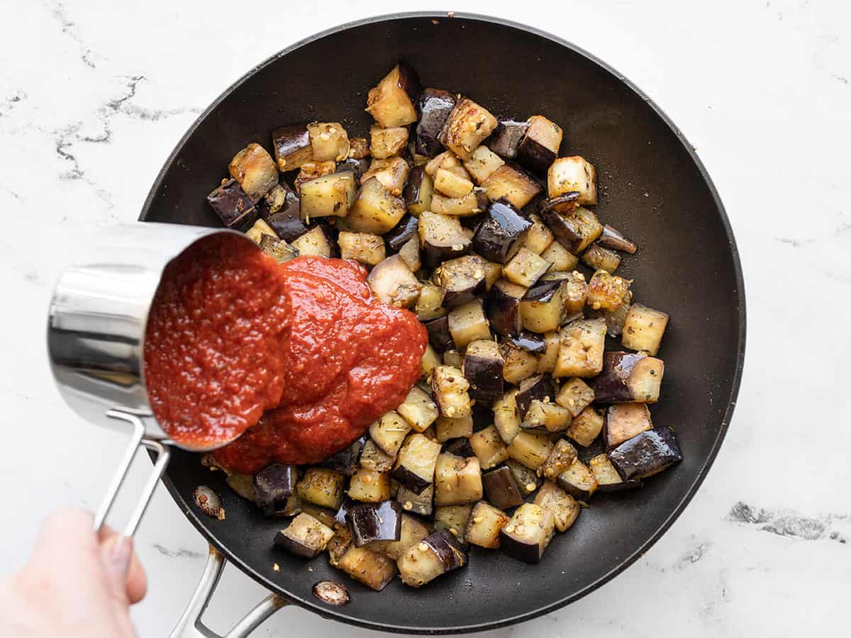 Marinara sauce being added to sautéed eggplant in the skillet