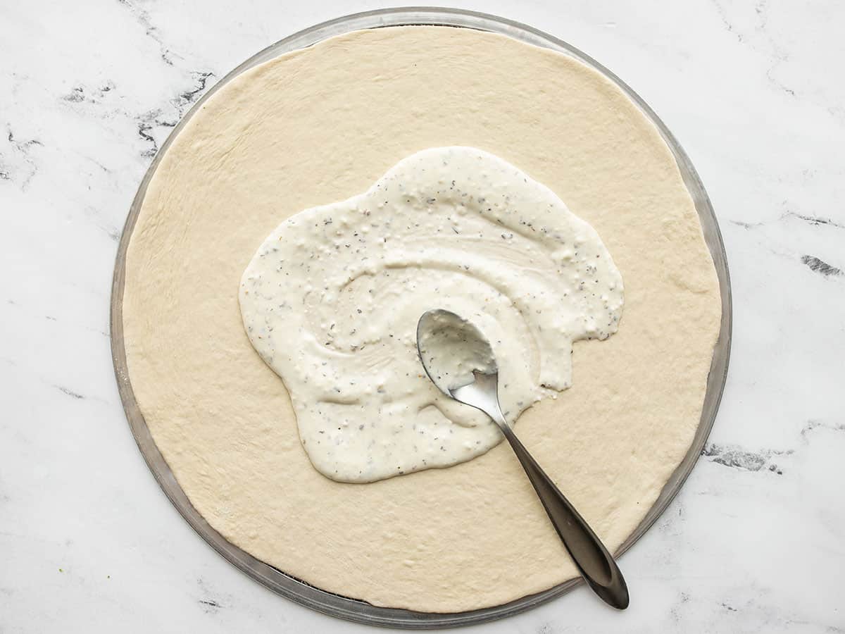 White sauce being spread onto pizza dough