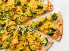One slice of broccoli cheddar pizza being pulled from the pie