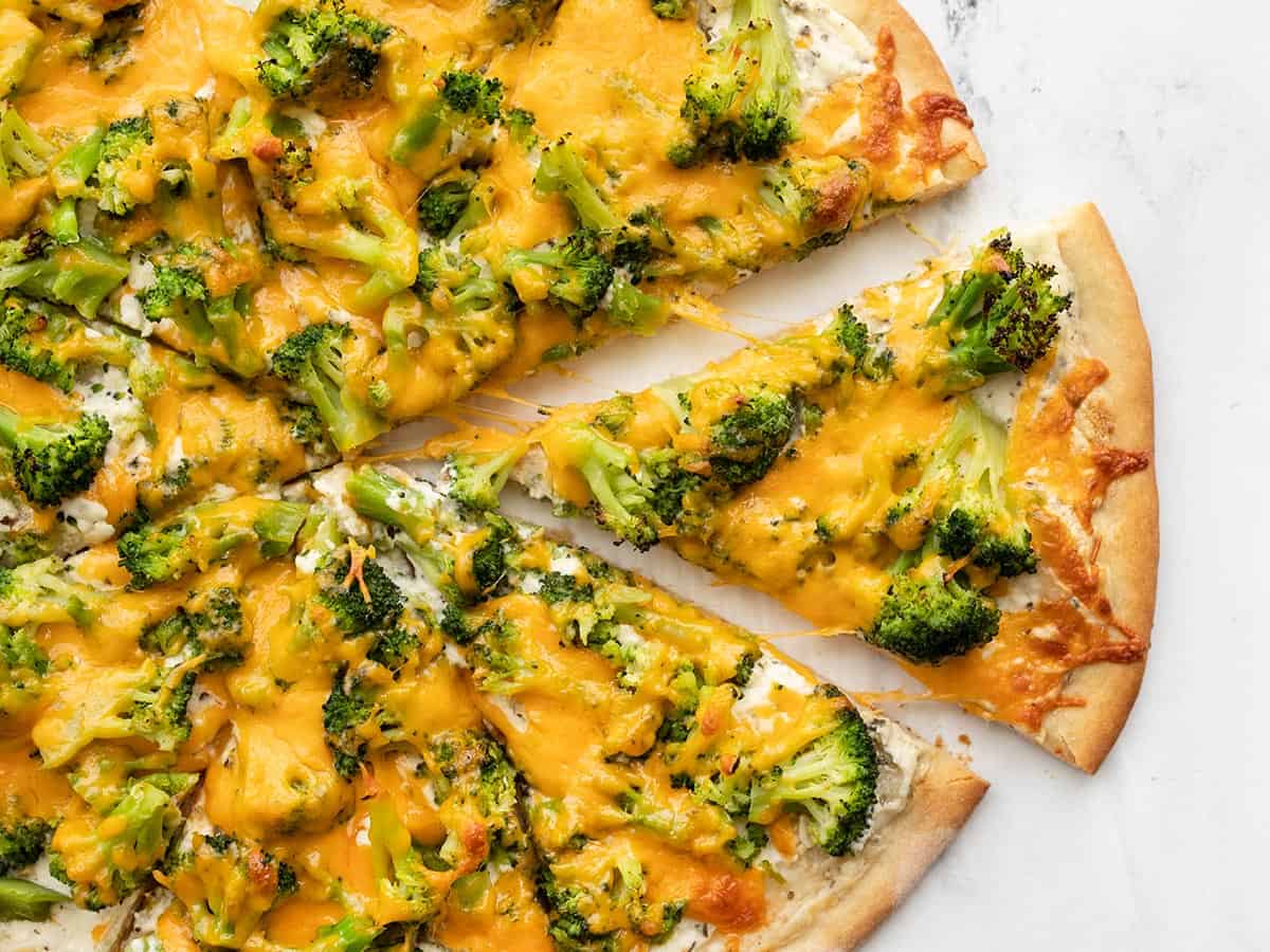 One slice of broccoli cheddar pizza being pulled from the pie