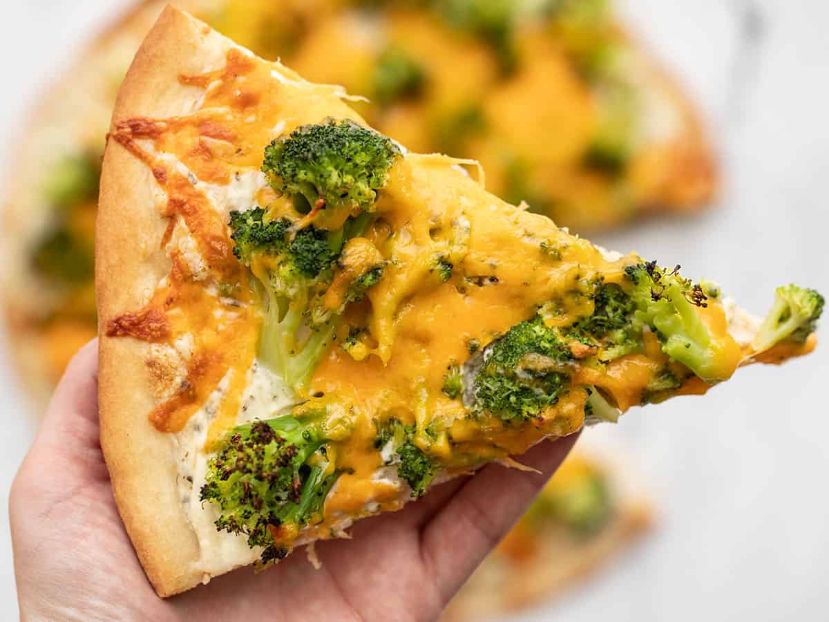 One slice of broccoli cheddar pizza being held close to the camera