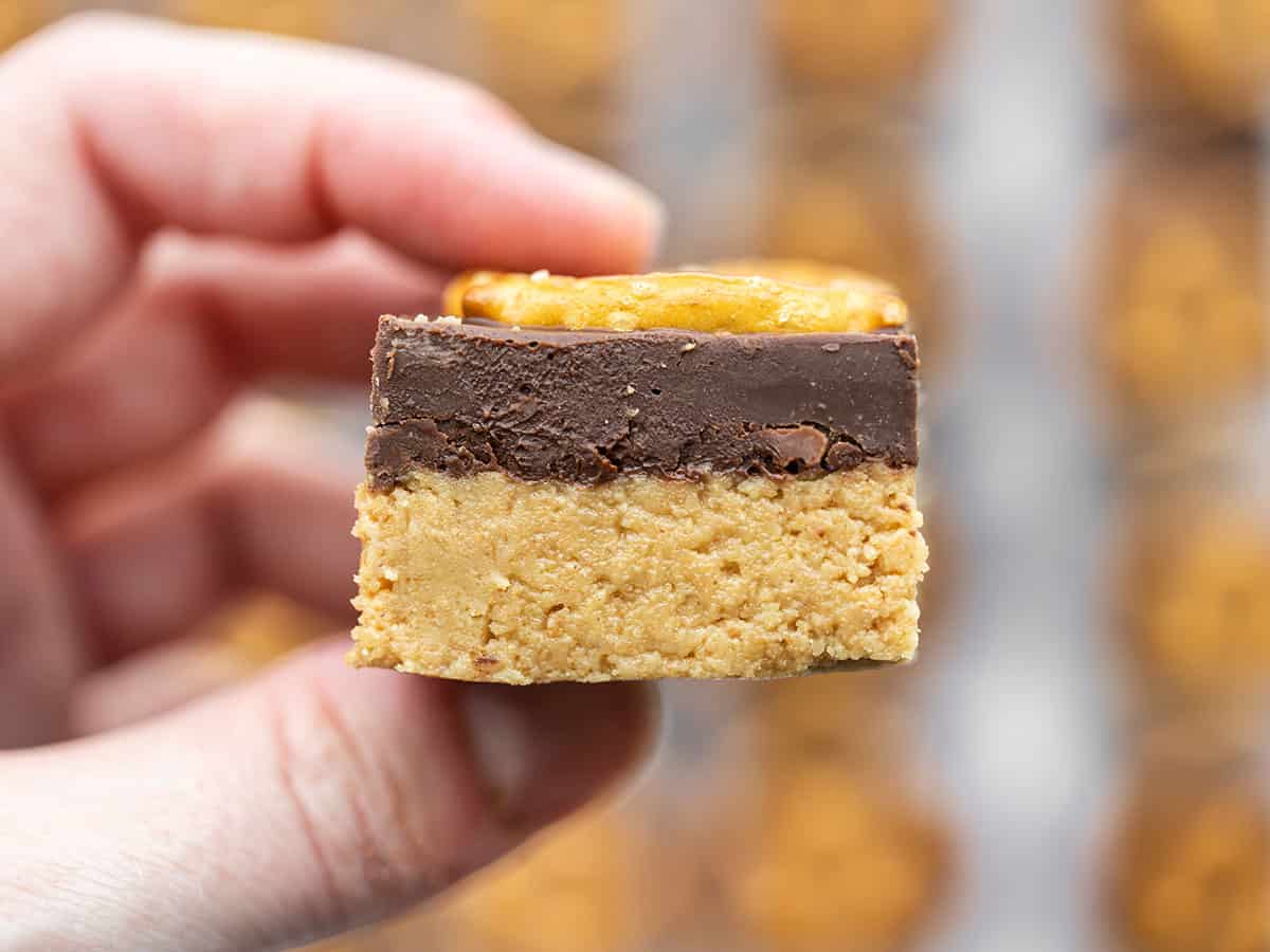 A hand holding one no bake peanut butter bar close to the camera so you can see the side
