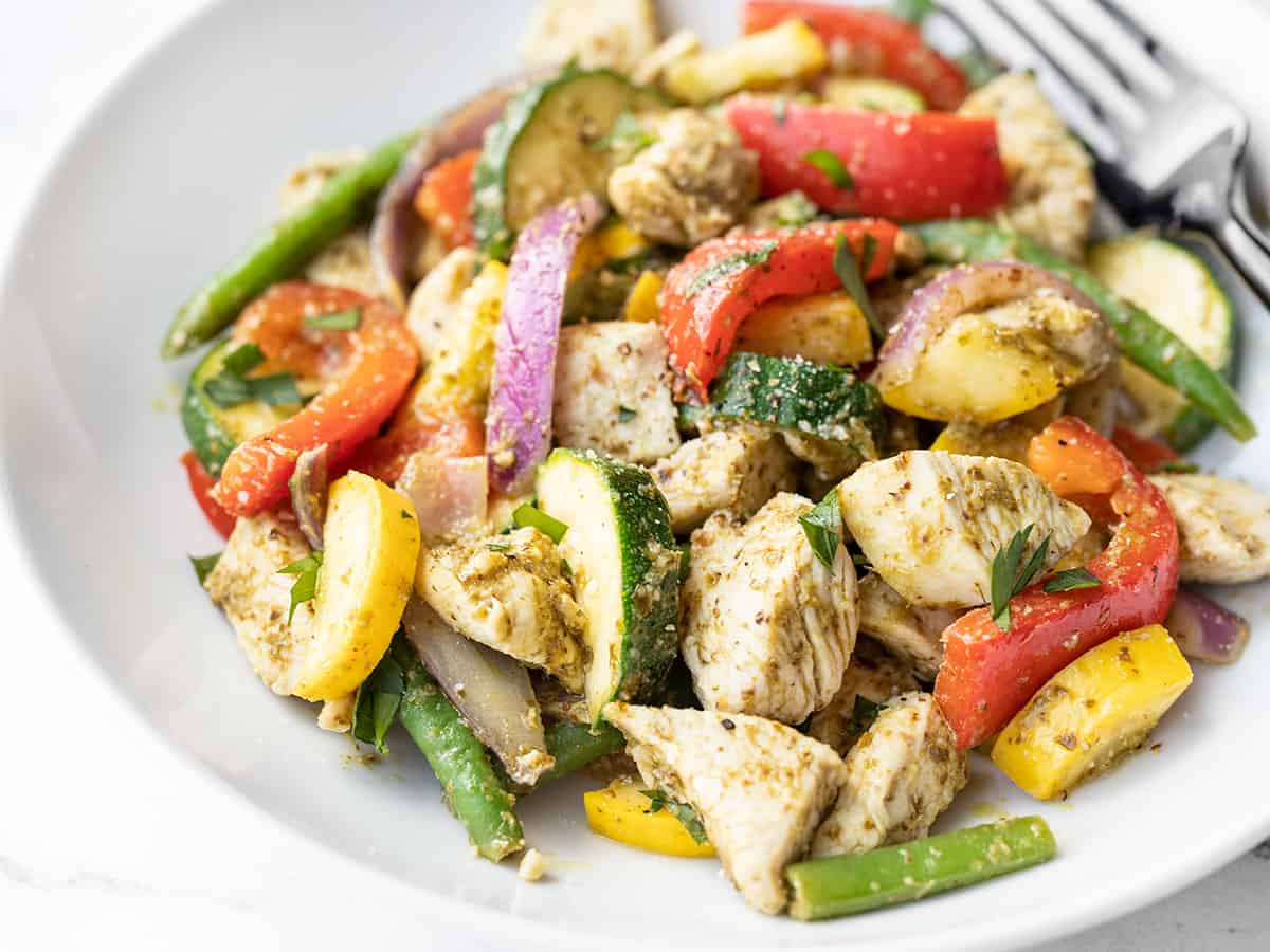 side view of a bowl full of pesto chicken and vegetables