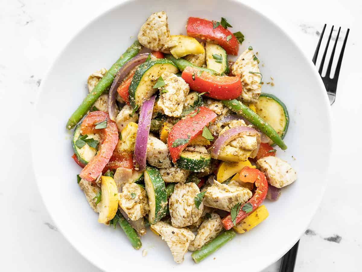 pesto chicken and vegetables in a bowl topped with a pinch of parmesan