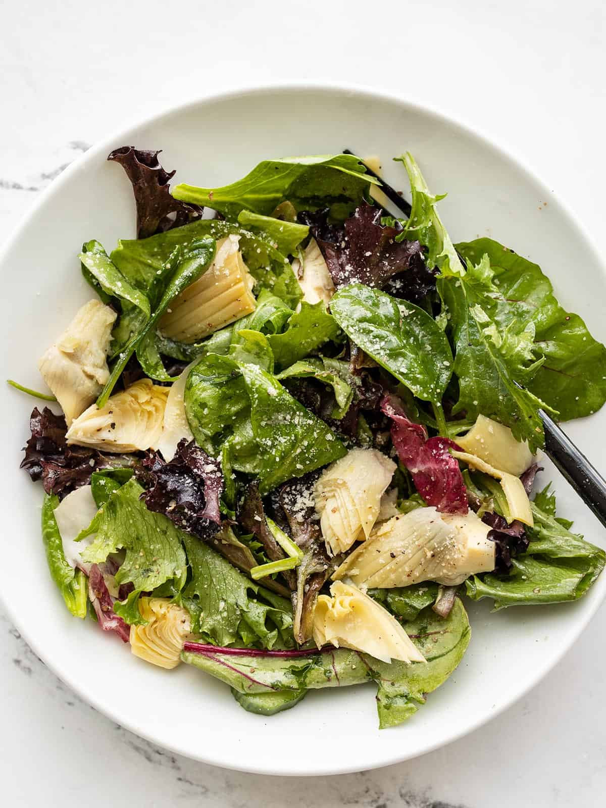 Overhead view of a simple side salad with artichokes in a white bowl