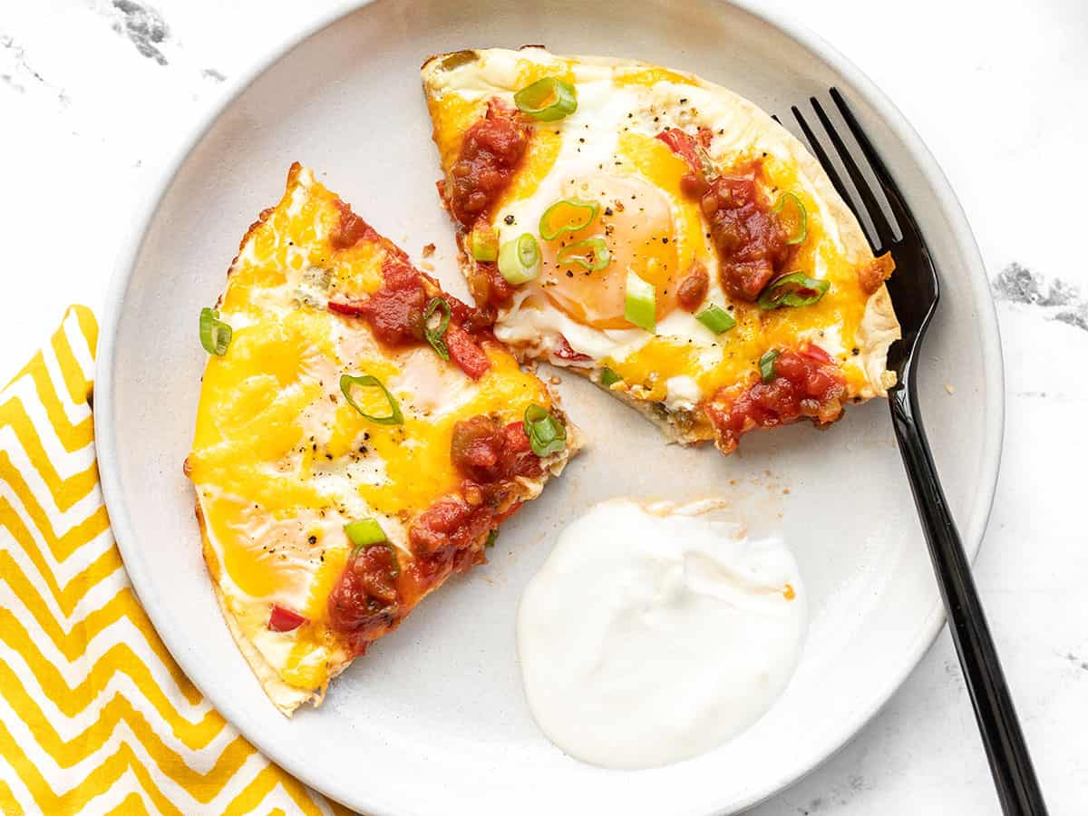 Southwest tortilla baked eggs on a plate with sour cream and a fork