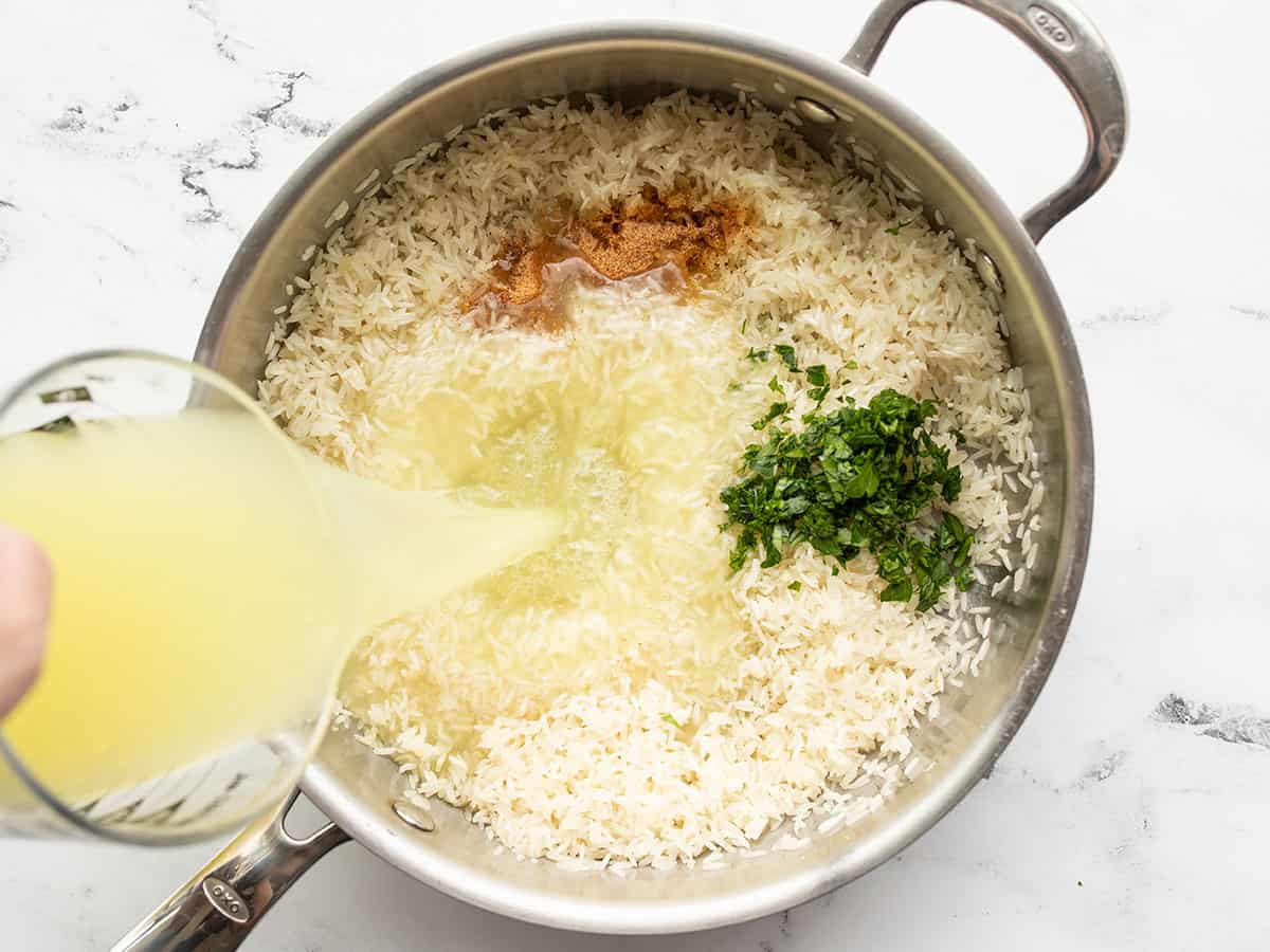 Broth being poured into the skillet with the rice, seasoning, and parsley
