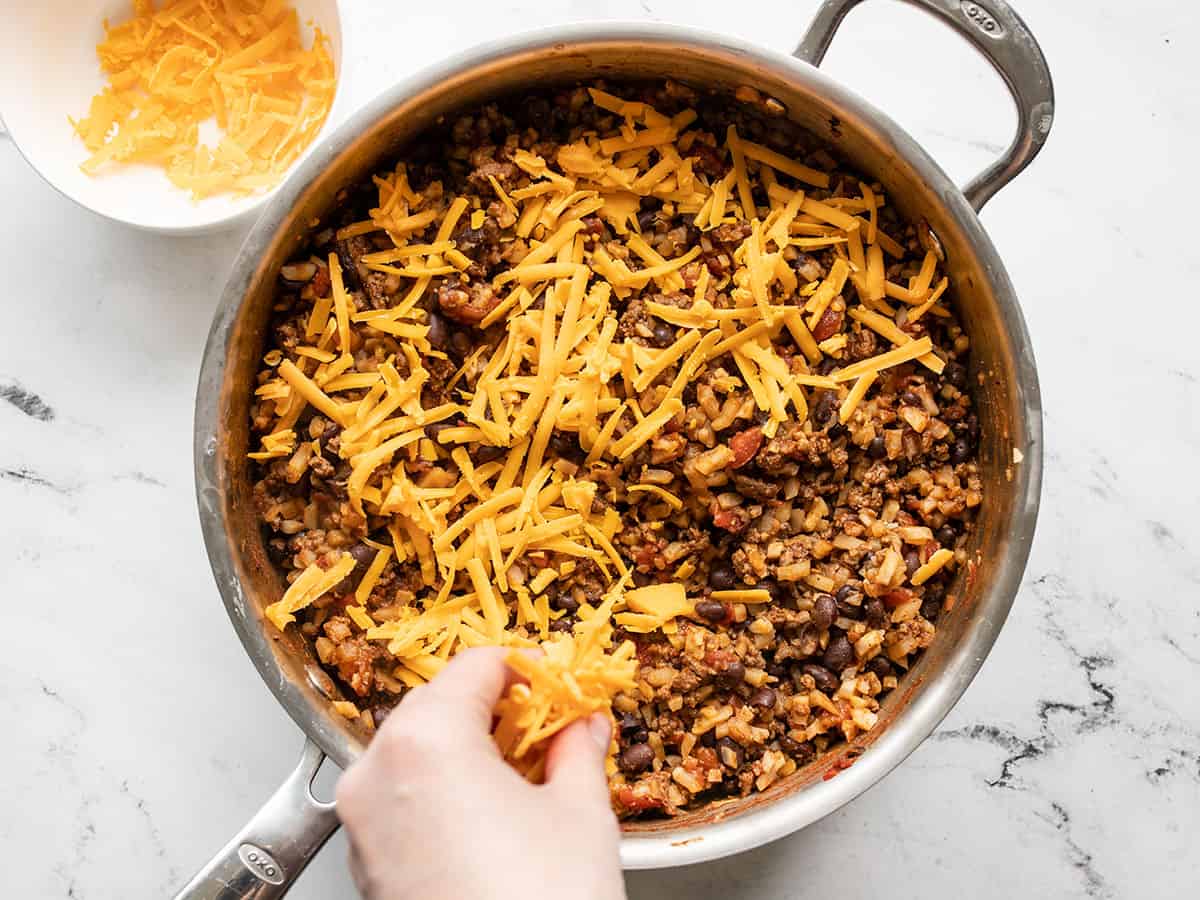 Shredded cheddar being added to the skillet