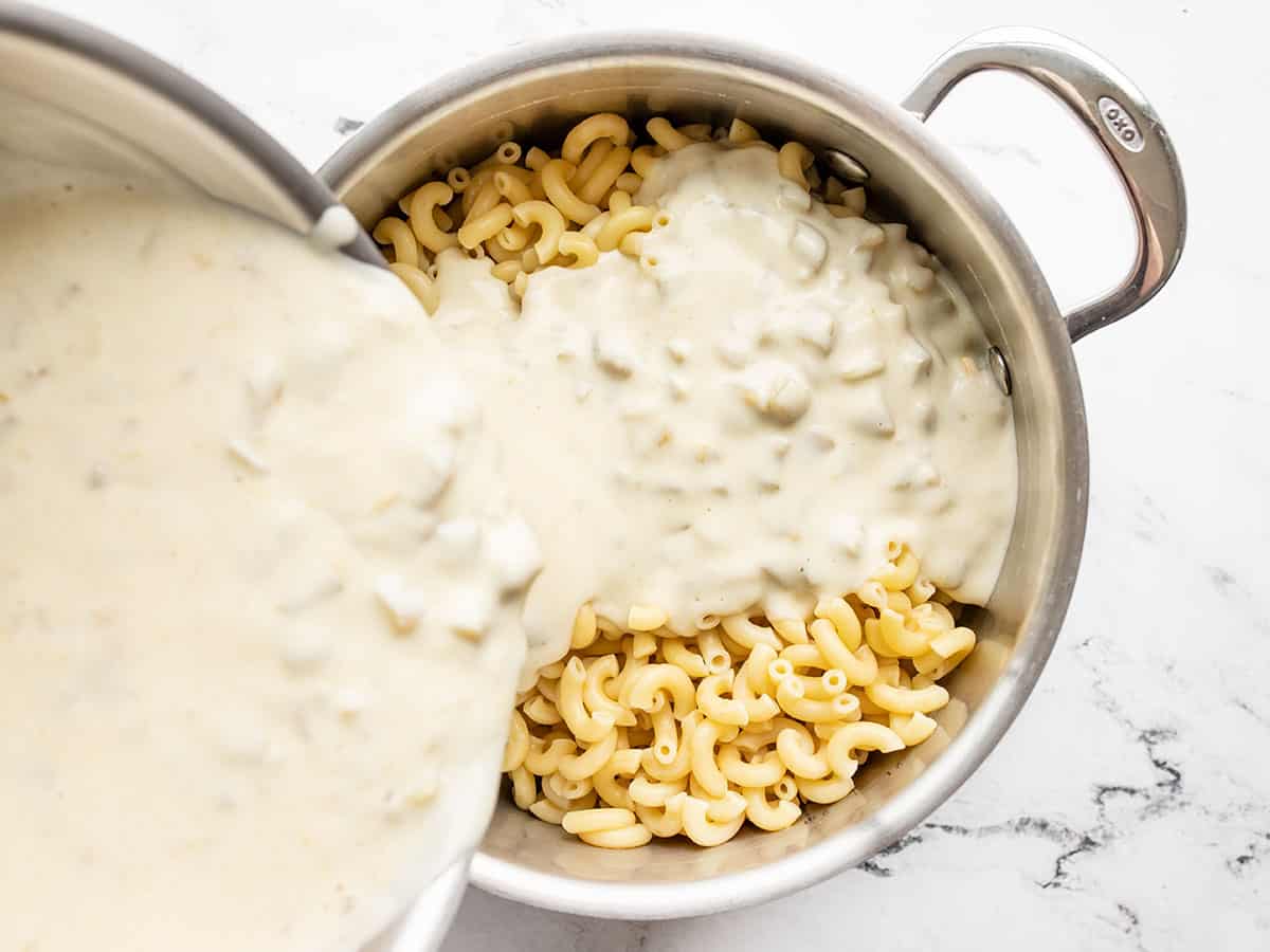 Cheese sauce being poured over the drained pasta