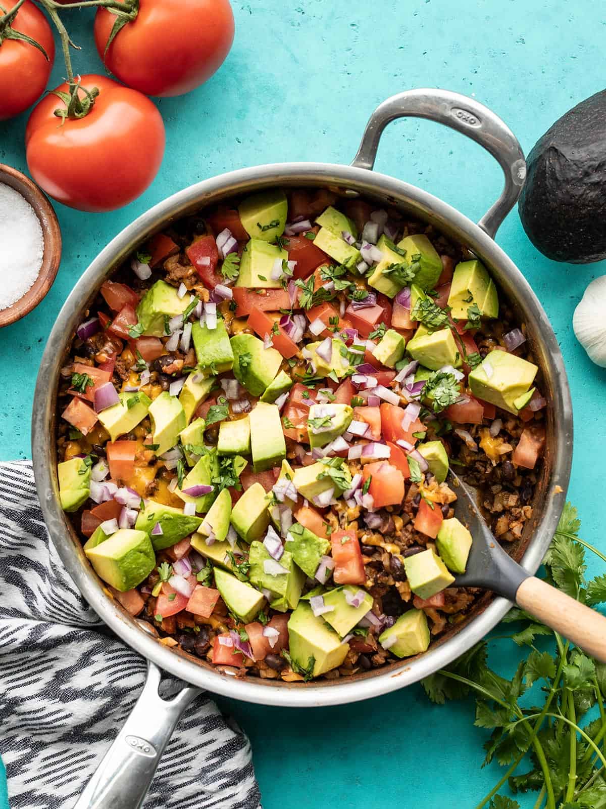 Overhead view of beef and cauliflower taco skillet with vegetables on the side and a spatula in the side