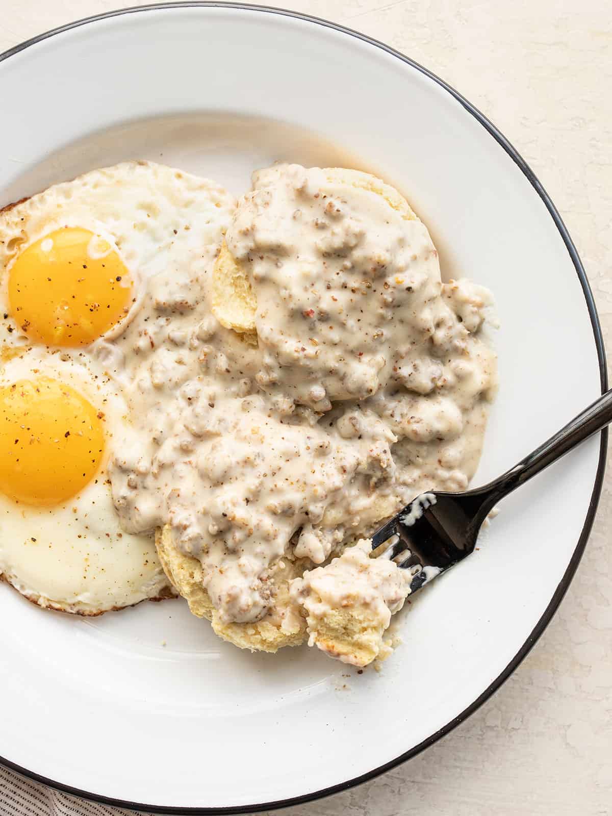 Biscuits and gravy on a plate with eggs, a fork taking a bite