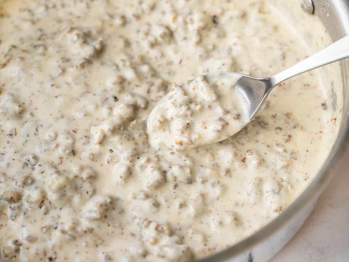 Close up of country sausage gravy in a skillet with a spoon lifting a bite