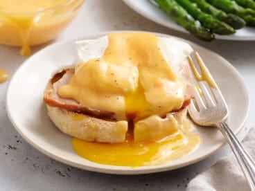 Hollandaise sauce on eggs and ham and an english muffin.