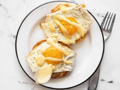 hollandaise sauce being drizzled over two eggs on English Muffins