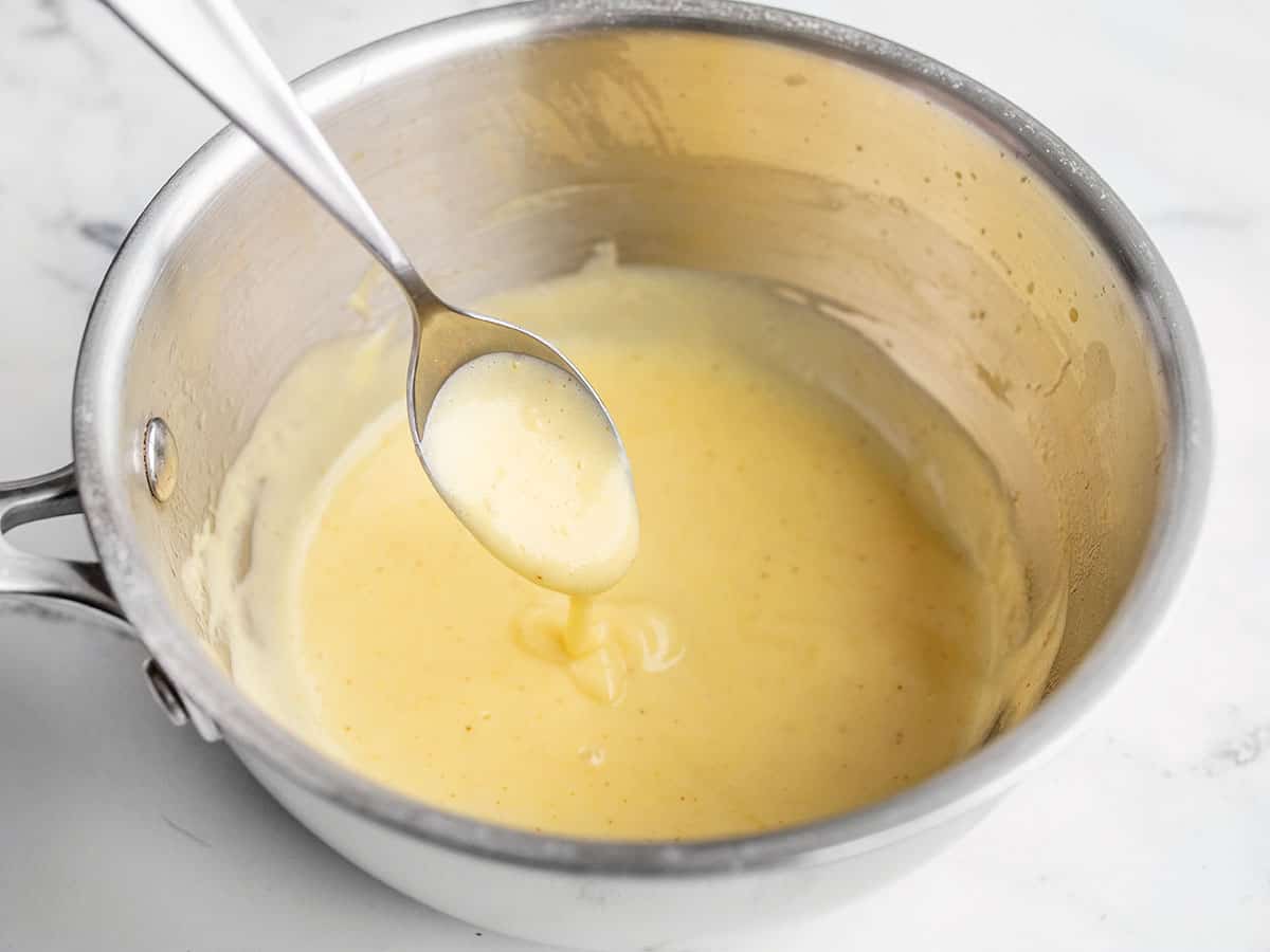 hollandaise sauce dripping off a spoon into a saucepot