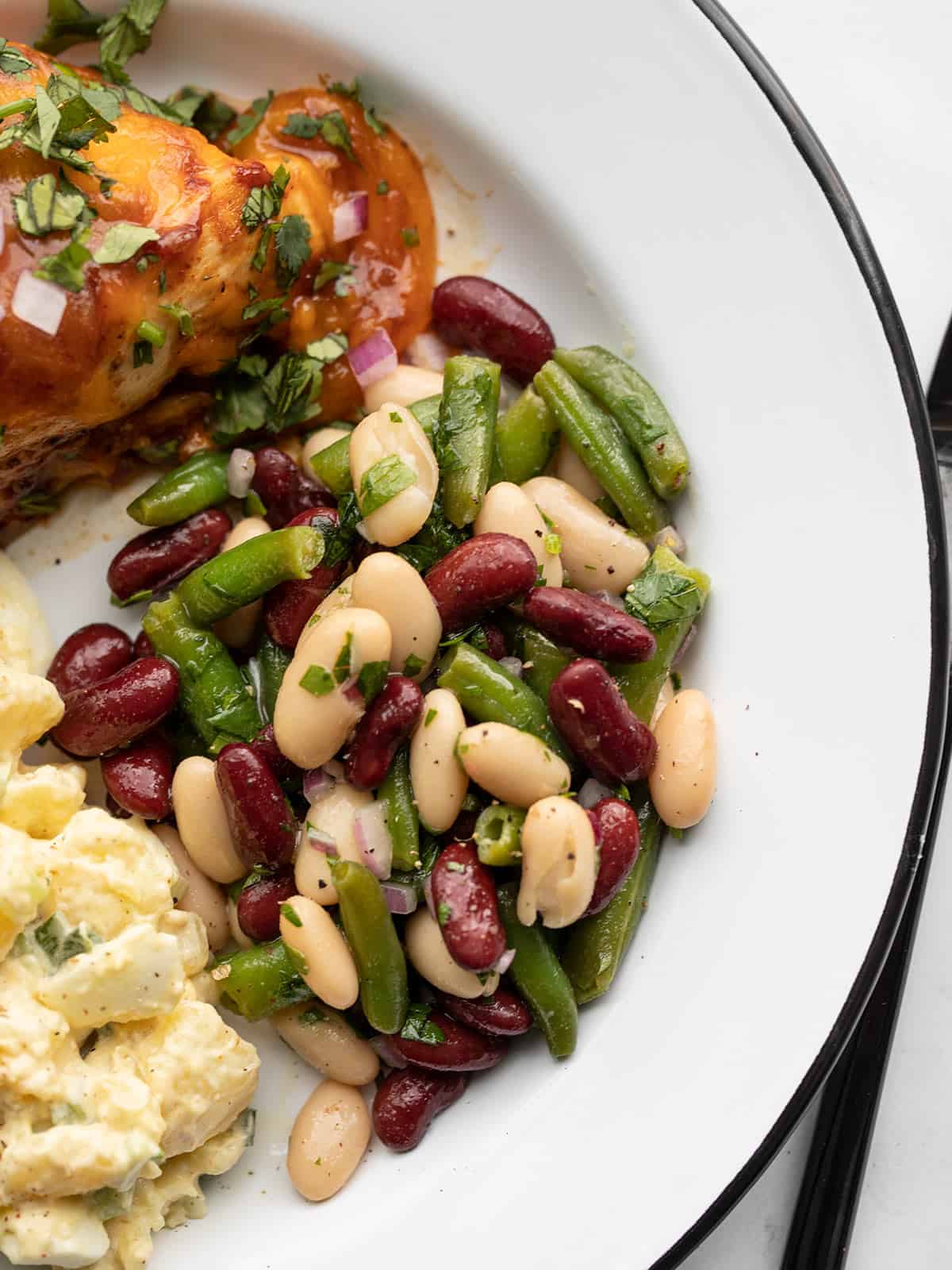 close up of three bean salad on a plate with bbq chicken and potato salad