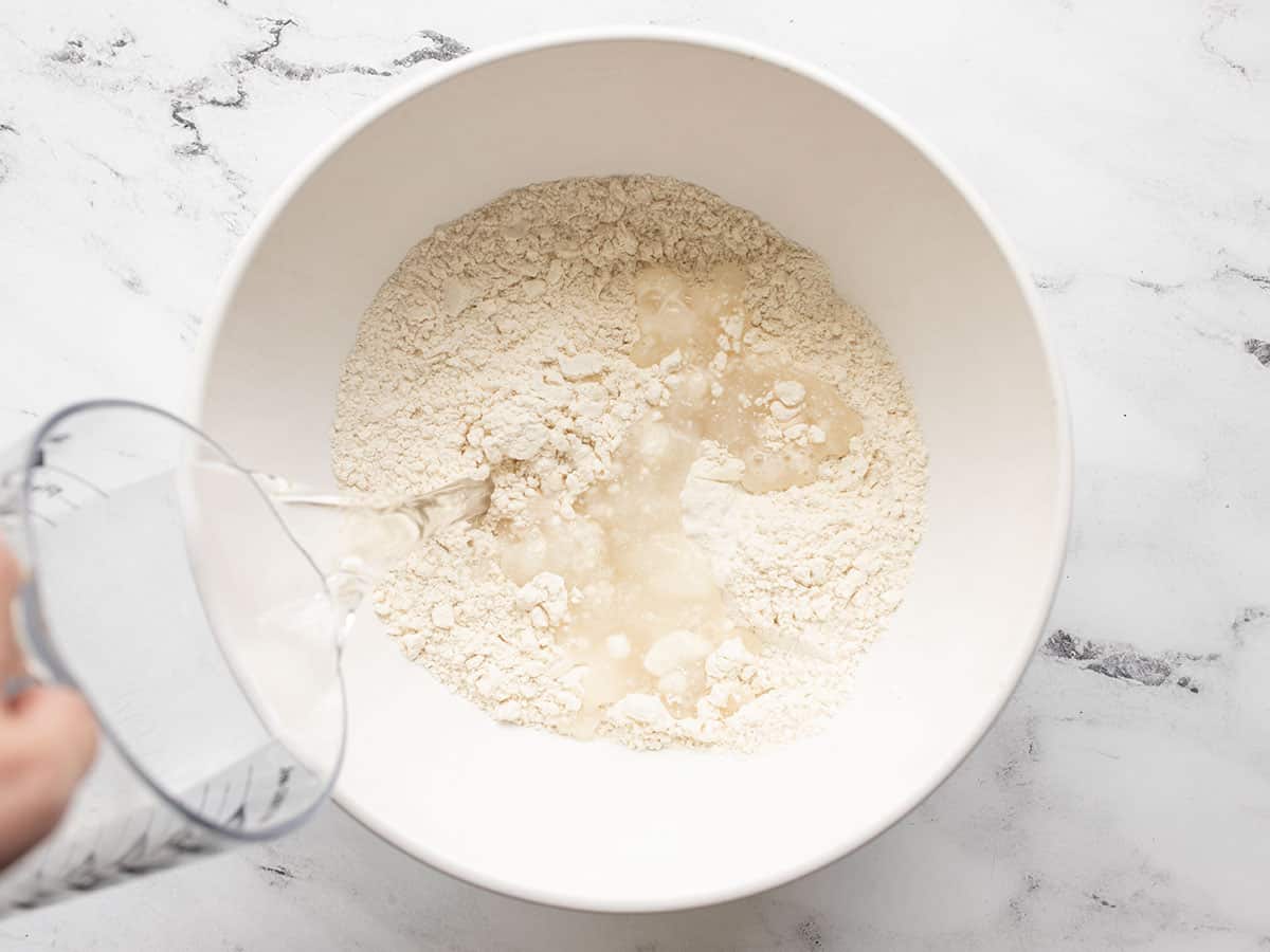 Water being poured into the bowl of flour