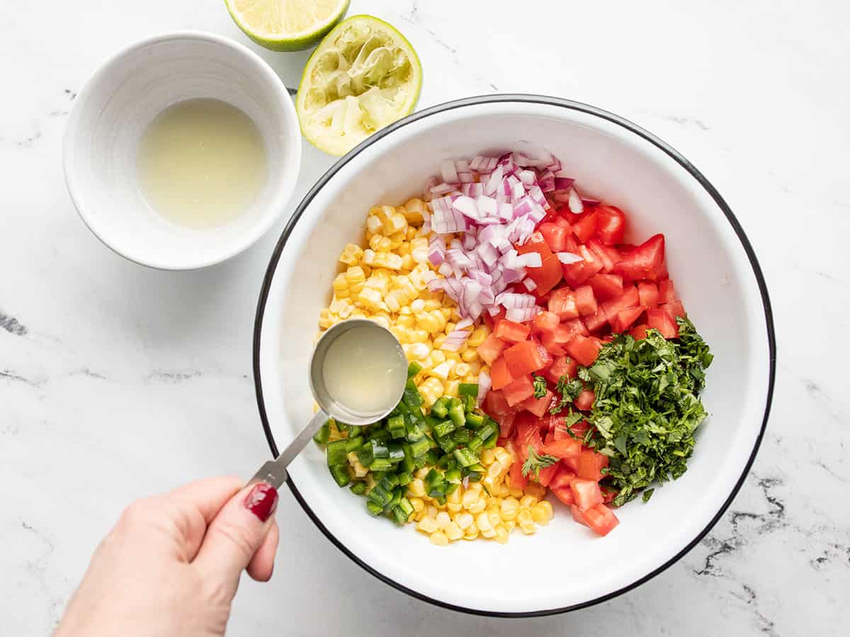 lime juice being drizzled over the bowl of salsa ingredients