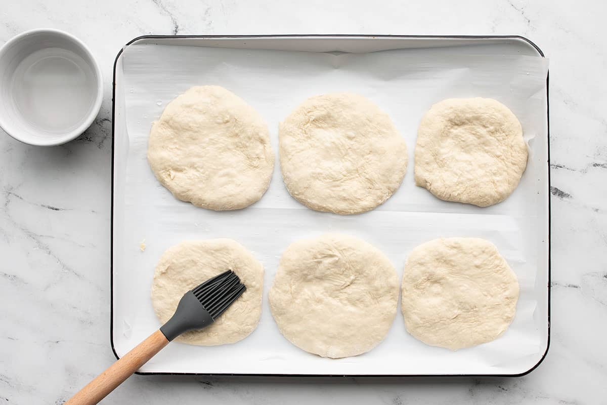 Water being brushed on top of the sandwich rounds