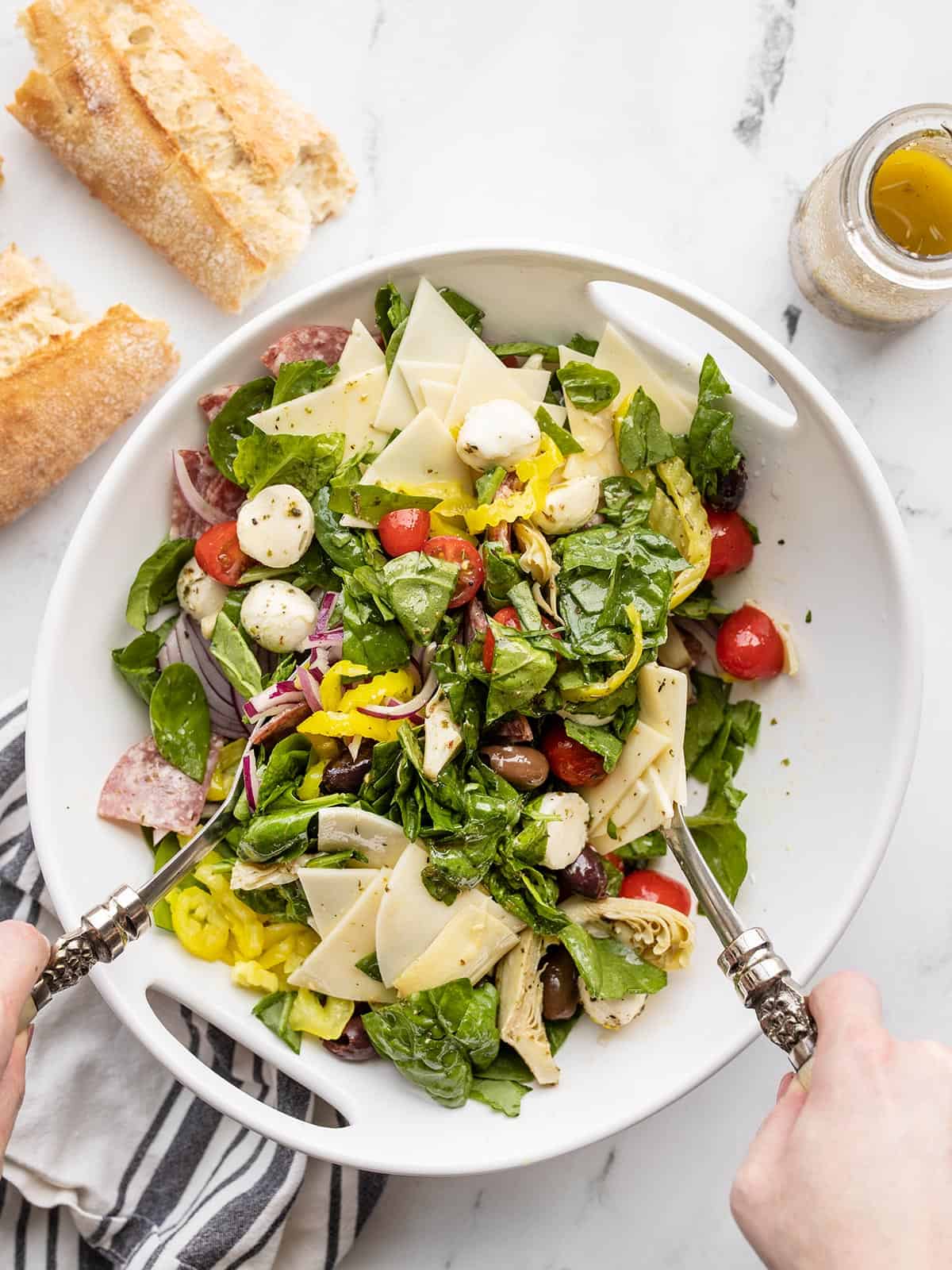 Antipasto salad being tossed with metal salad tongs