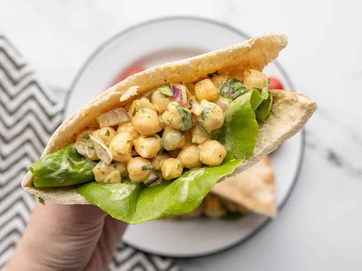 A hand holding a pita stuffed with curry chickpea salad