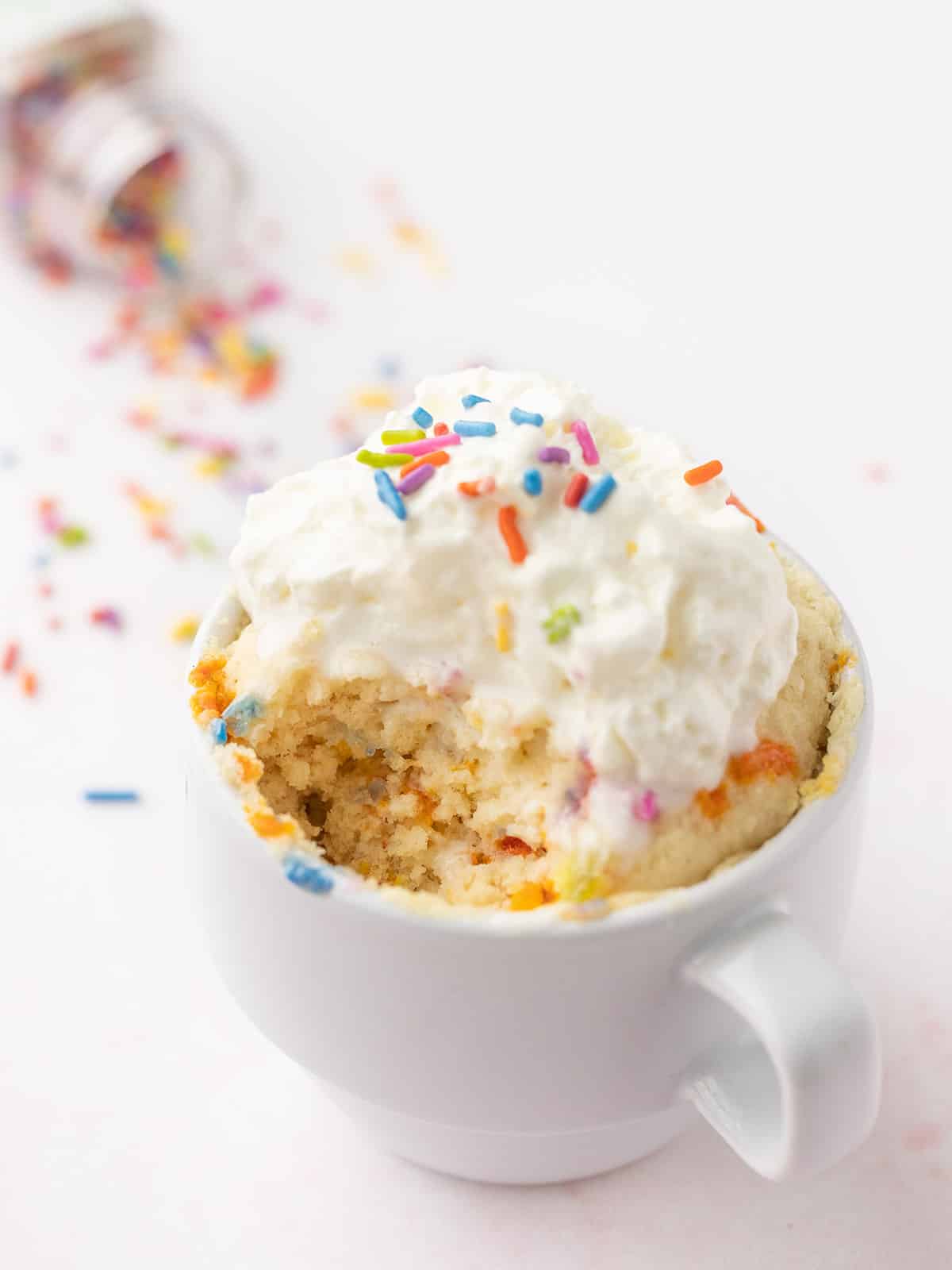 A funfetti mug cake topped with whip cream, a scoop taken out of the side