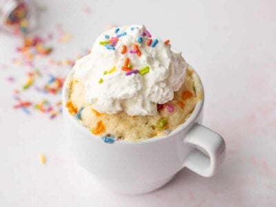 A Funfetti Mug Cake topped with whipped cream from the side