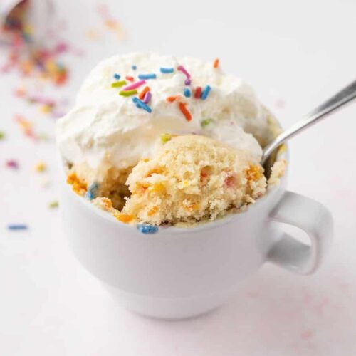 a spoon lifting a bite of the funfetti mug cake out of the mug