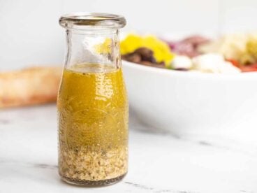 Italian dressing in a glass carafe in front of a bowl of salad