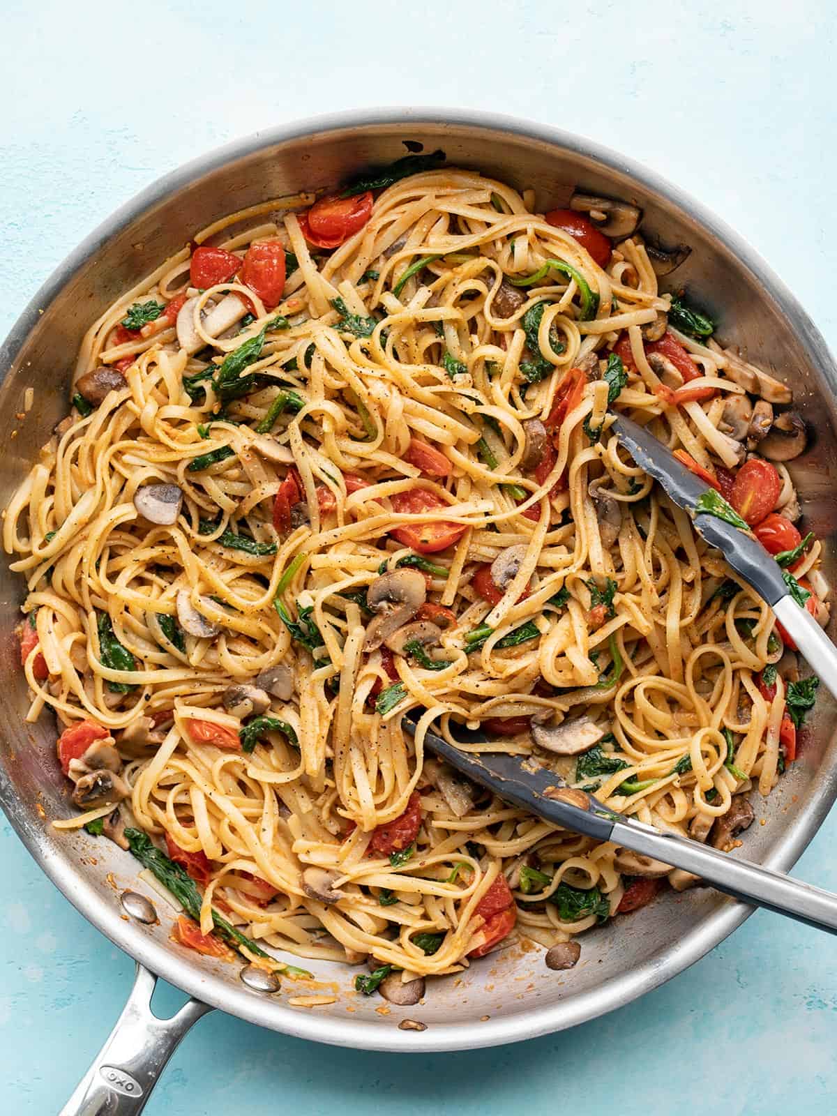 Overhead view of quick veggie pasta in a skillet with tongs