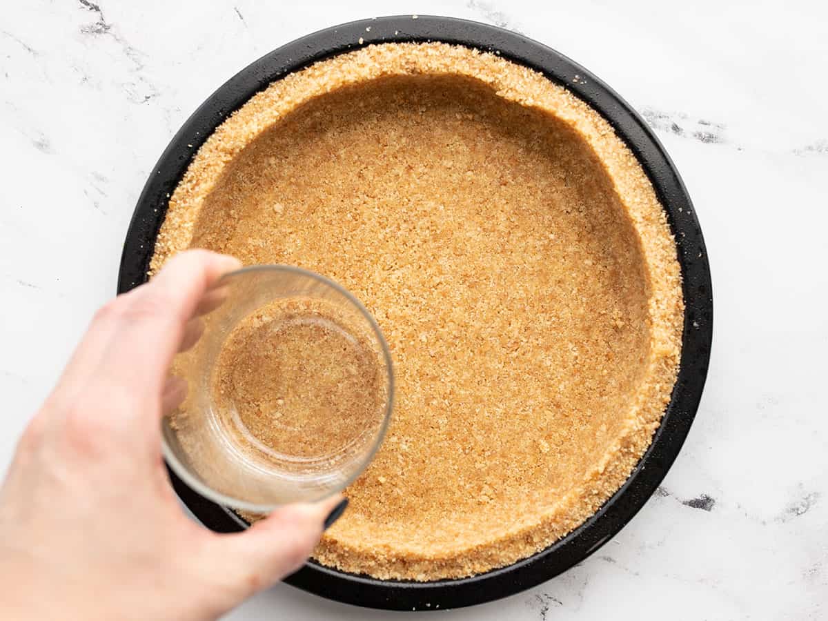 Vanilla wafer crust being pressed into the pie plate with a glass