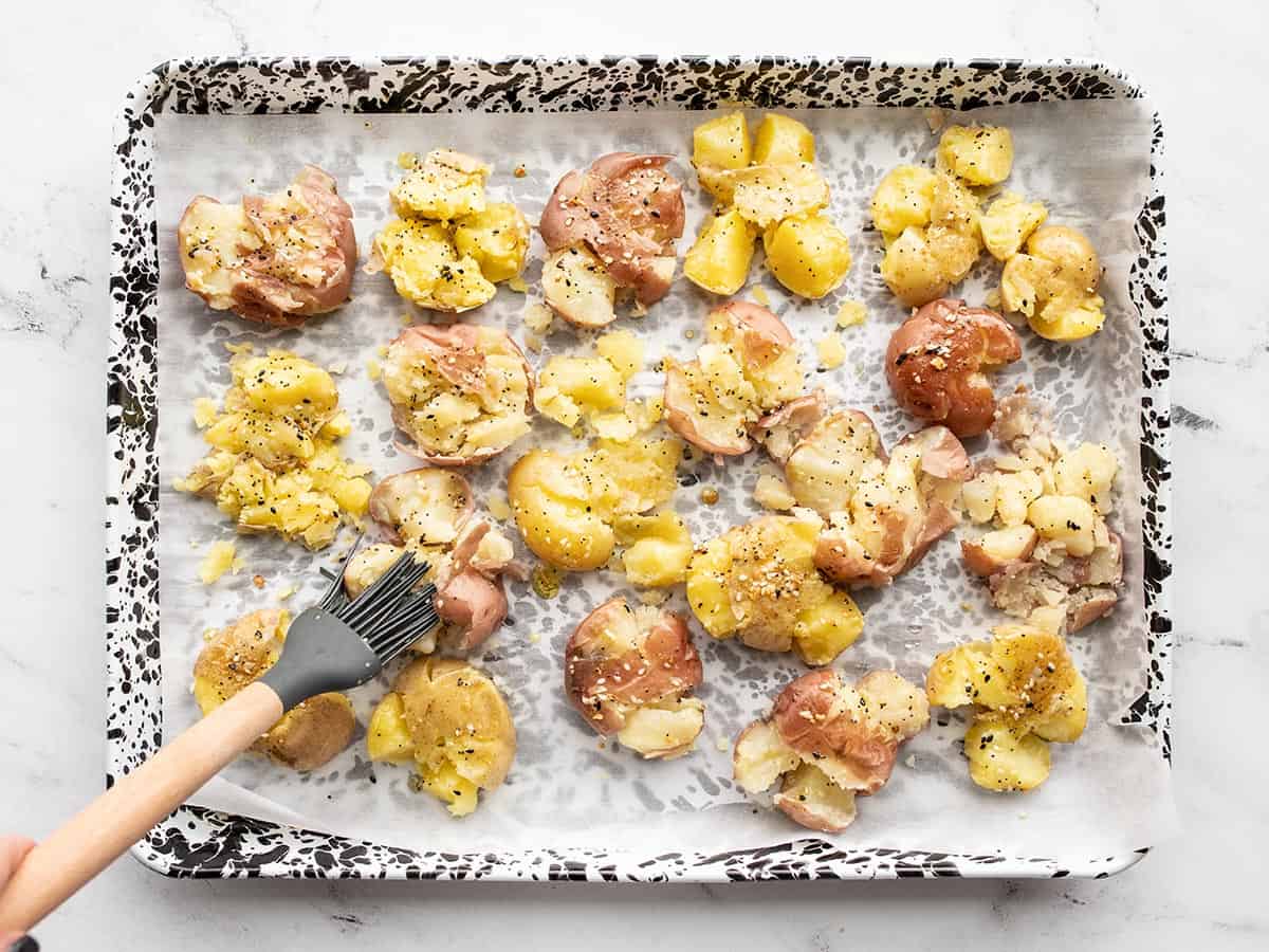 Seasoned oil being brushed over the smashed potatoes