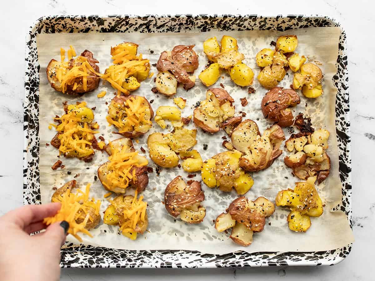 Baked smashed potatoes being topped with cheese