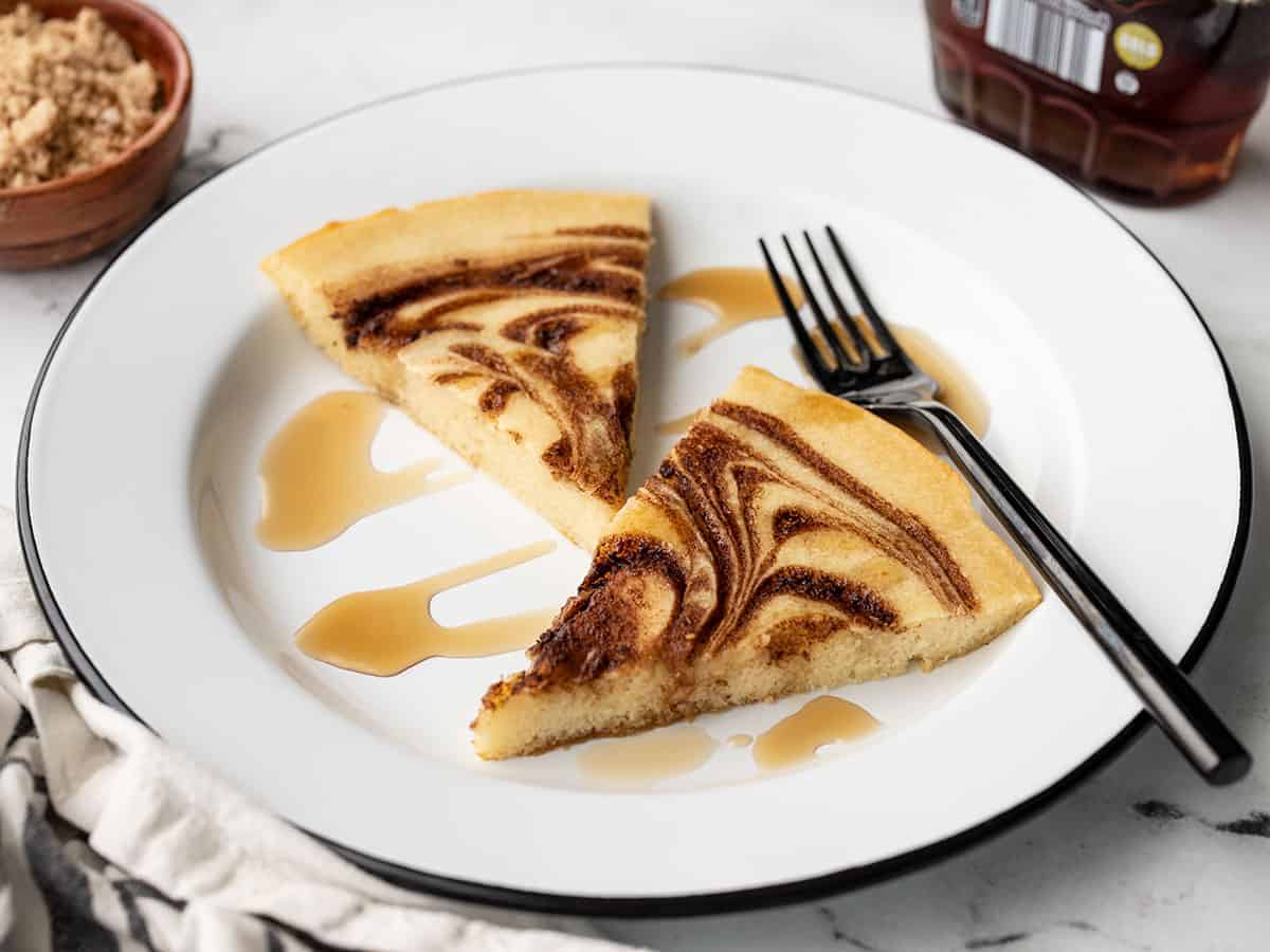 front view of two slices of oven pancake on a plate with maple syrup and a fork