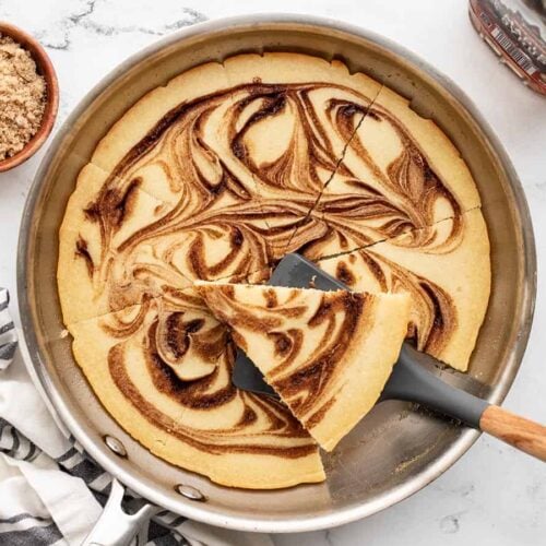 cinnamon swirl oven pancake with one slice on a spatula on the skillet