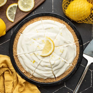 Overhead view of a sliced lemon cream pie with lemons on the sides