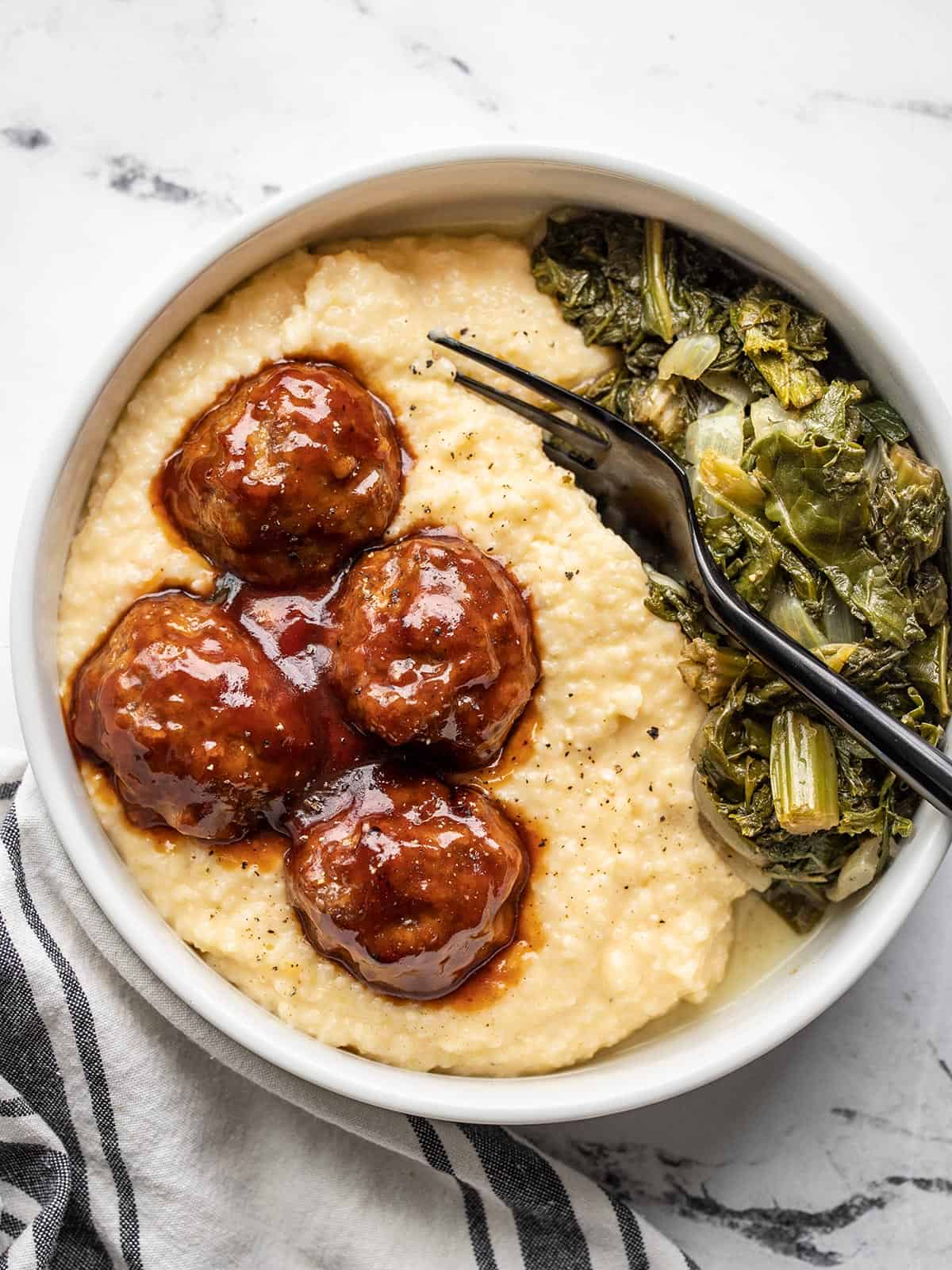 Overhead view of a bowl of cheese grits with bbq meatballs and collard greens