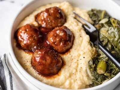 side view of bbq meatballs and cheese grits in a bowl with collard greens