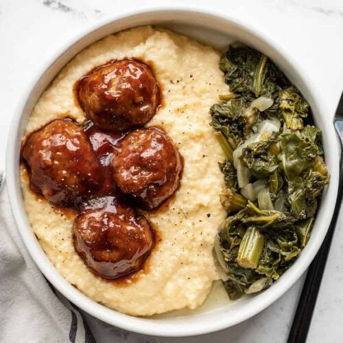 Overhead view of a bowl of cheese grits with bbq meatballs and collard greens