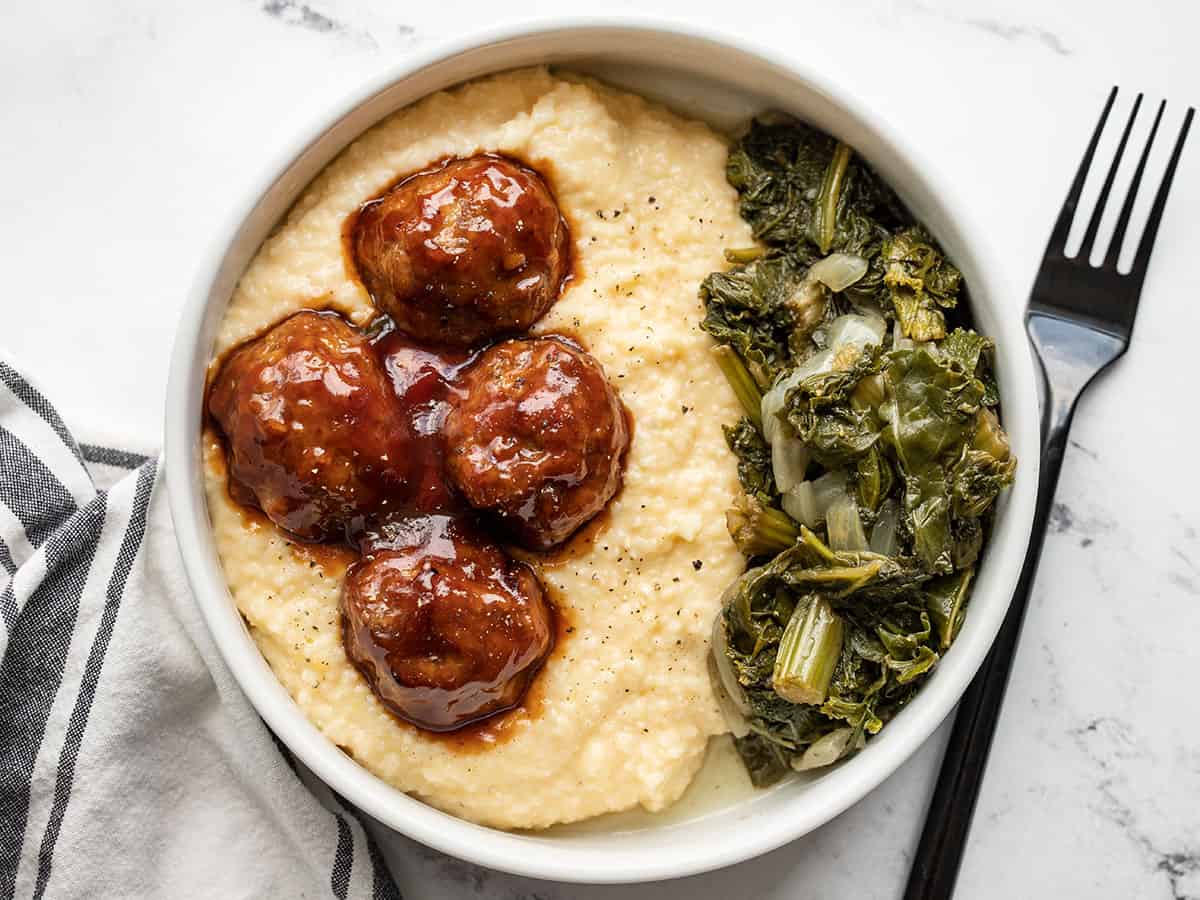 Overhead view of a bowl of cheese grits with bbq meatballs and collard greens