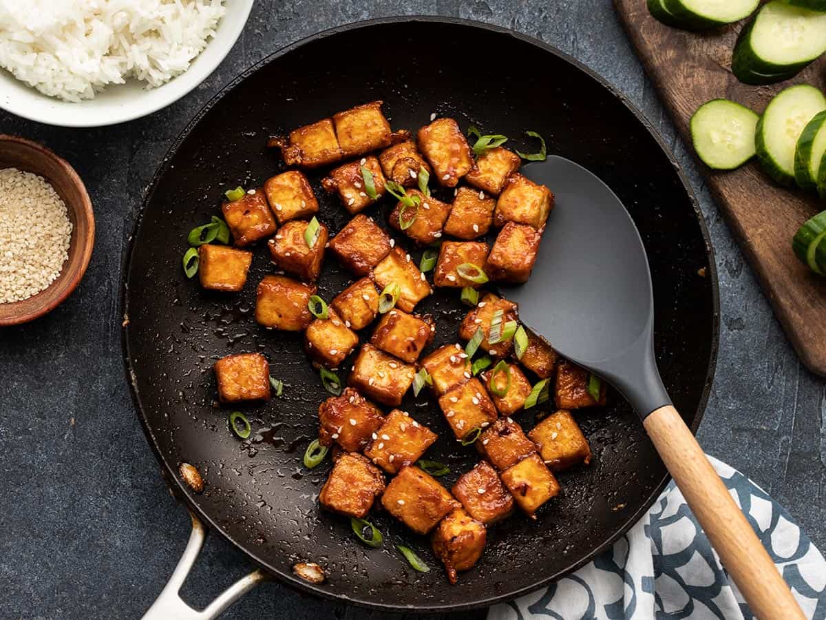 Honey sriracha tofu in the skillet with a spatula, ingredients on the sides