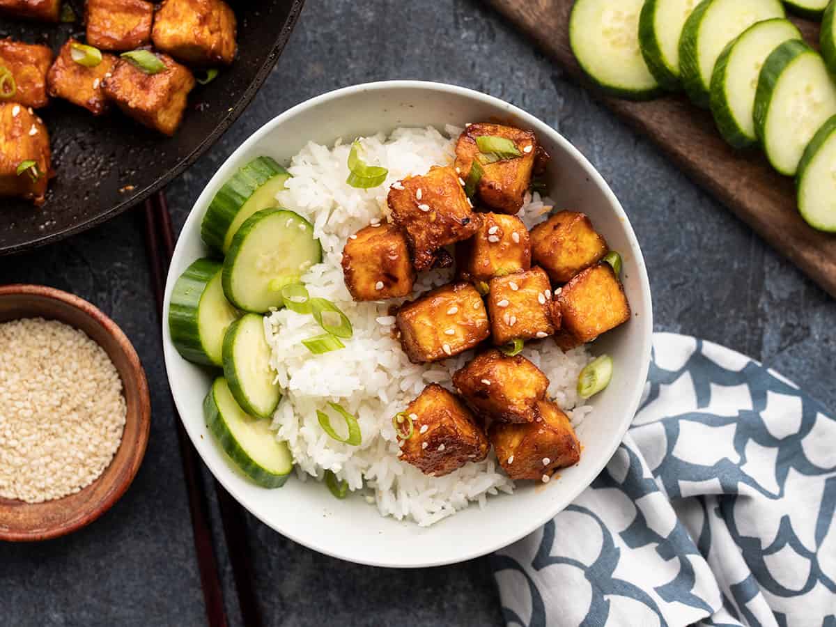 honey sriracha tofu in a bowl with rice, cucumber, and sesame seeds