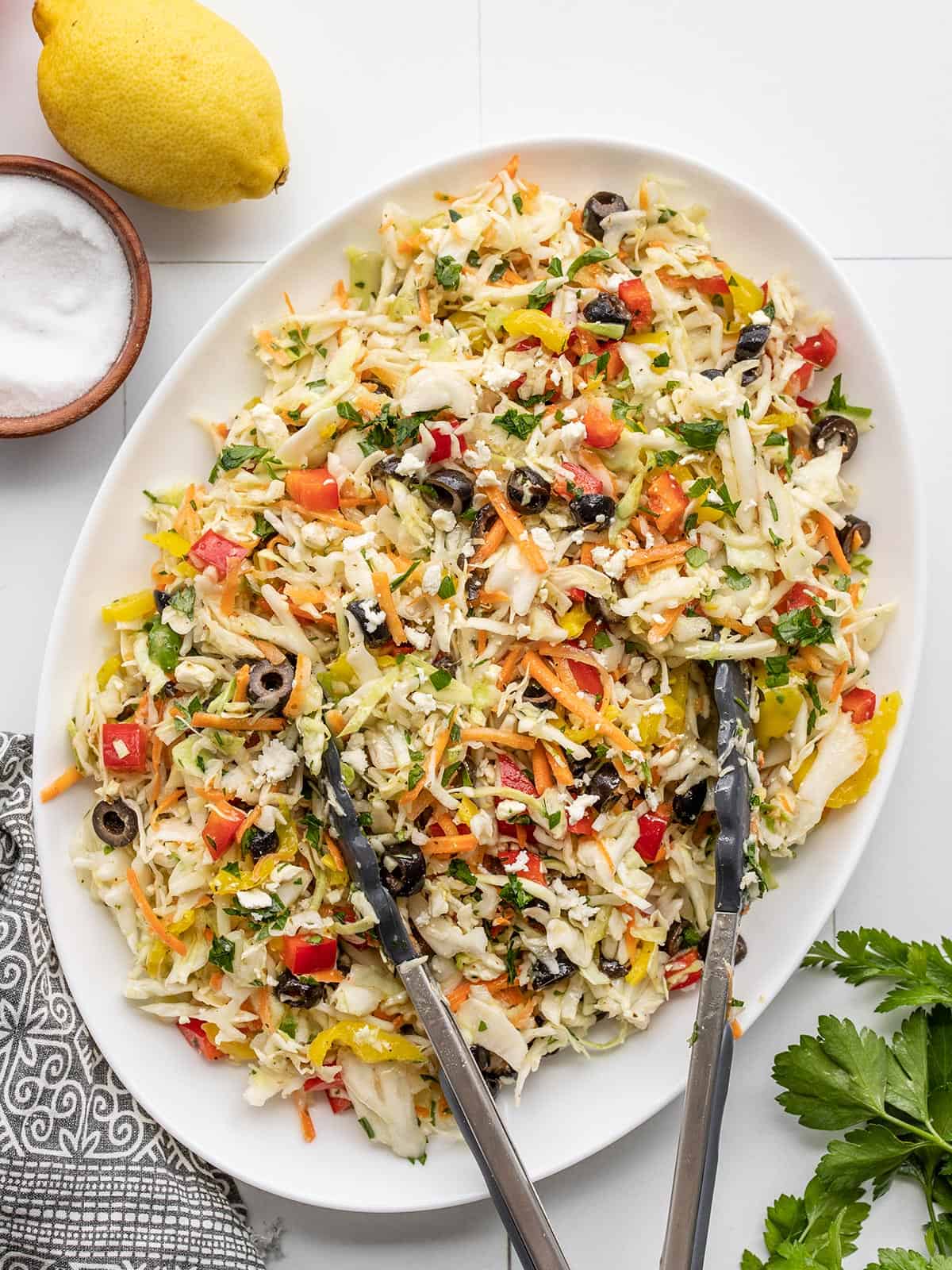 Overhead view of an oval serving dish with mediterranean coleslaw and tongs