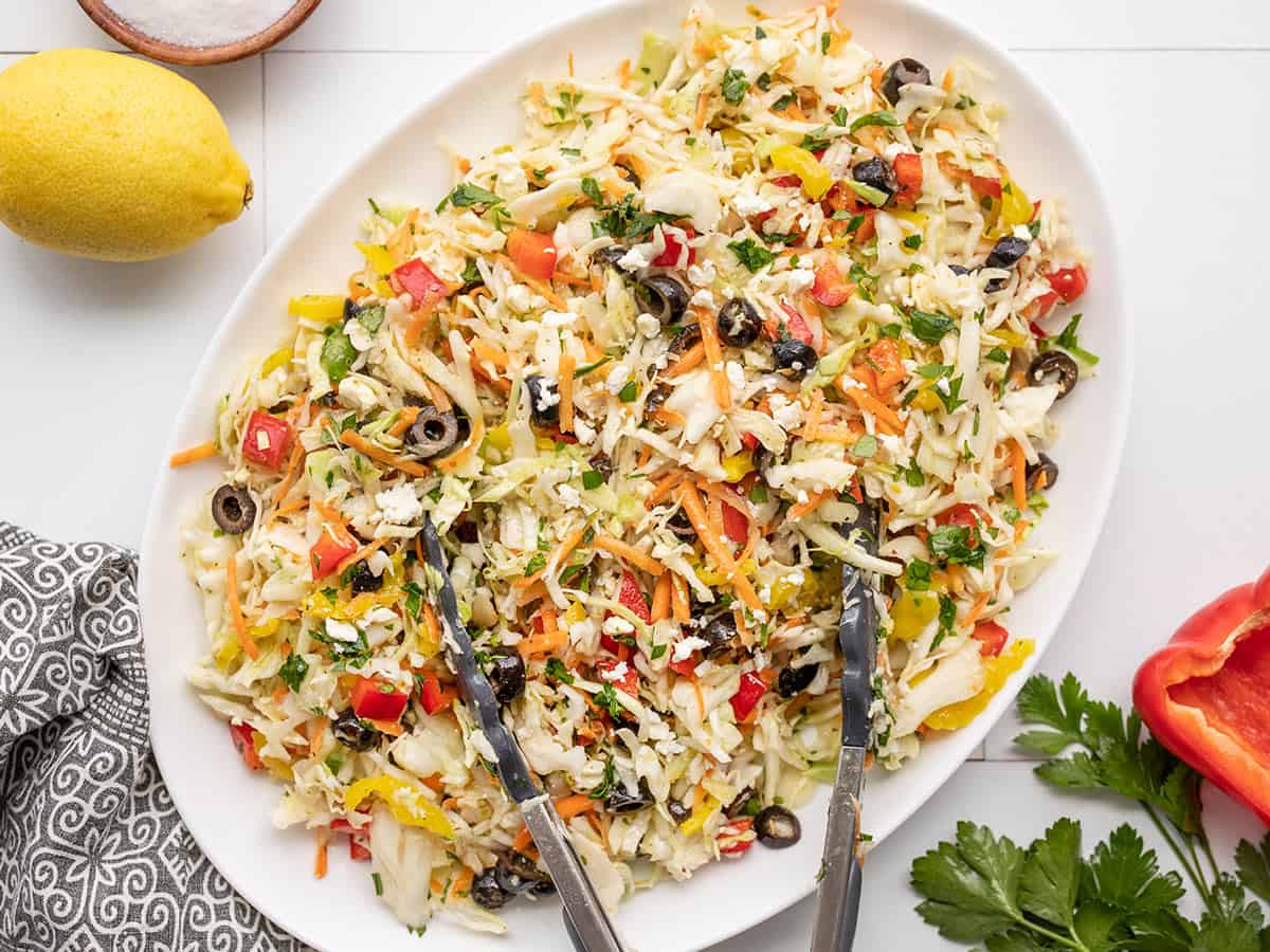 Overhead view of mediterranean coleslaw in an oval serving dish with tongs in the side