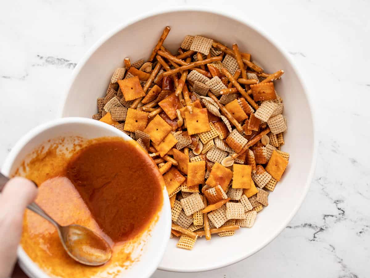 seasoned butter being poured over the snack mix