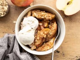 Apple crisp in a bowl topped with vanilla ice cream
