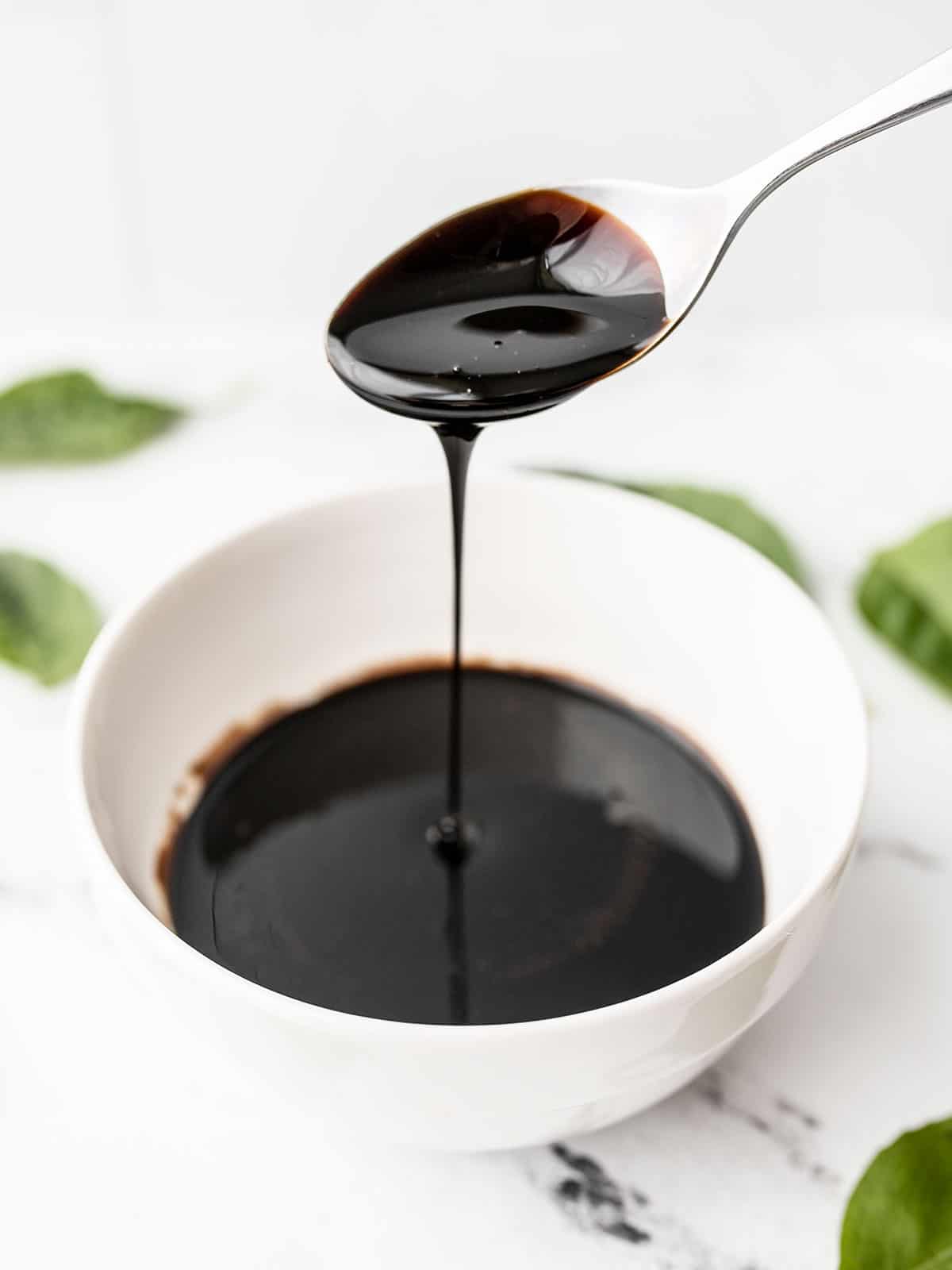 Balsamic glaze dripping off a spoon into a small bowl