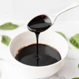 Balsamic glaze dripping off a spoon into a small dish, basil leaves all around